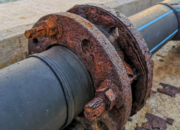 Foto mostra um cano de zona portuária enferrujado, simbolizando a poluição por metais