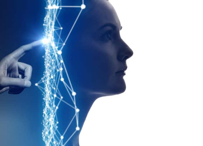 Imagem conceitual mostra uma mão tocando com o indicador a parte de trás da cabeça de uma mulher, com traços digitais azuis entre um e outro. A ideia é simbolizar a inteligência artificial
