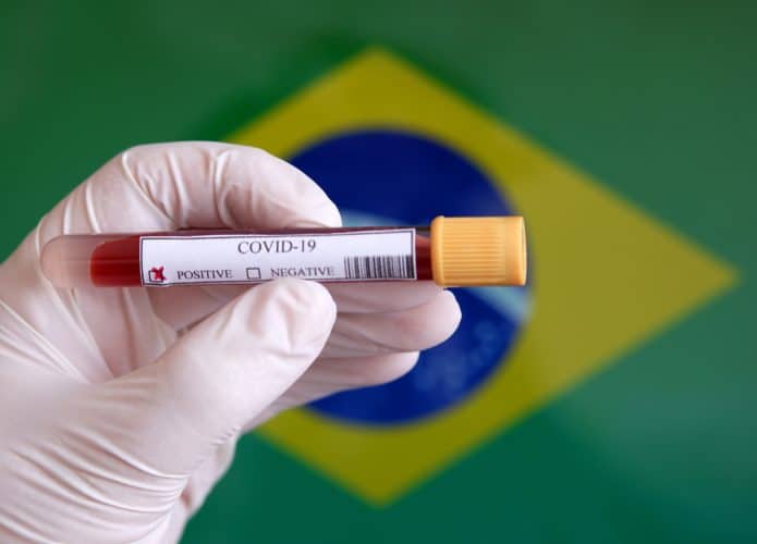 Bandeira do Brasil ao fundo de um teste positivo de Covid-19