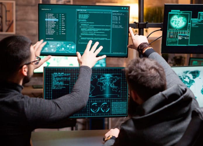 dois hackers apontando para telas com código