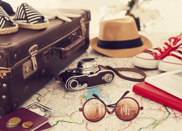 Mala, binóculos, chapéu e mala de viagem em cima de um mapa