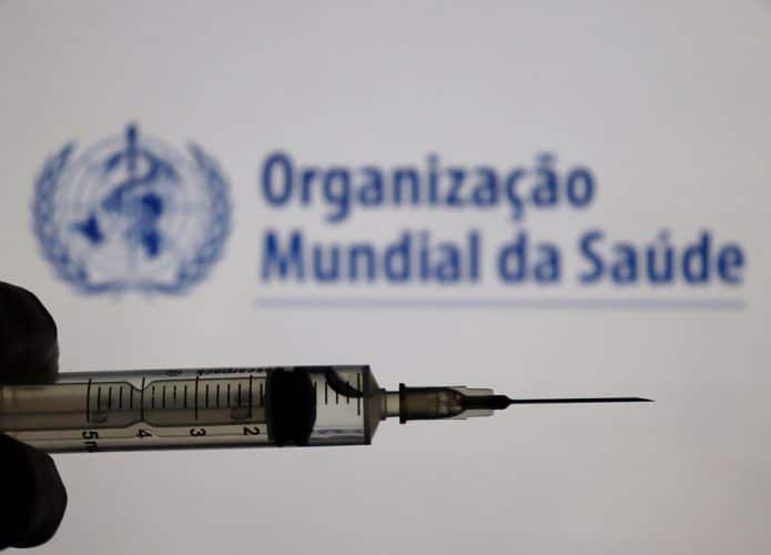 Logo da OMS ao fundo de uma mão segurando uma seringa