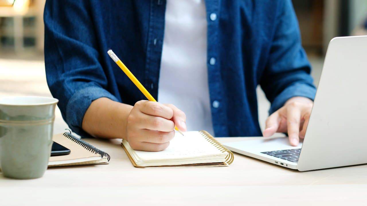 Pessoa estudando com caderno e computador