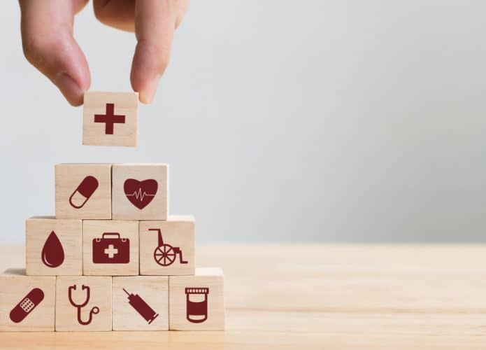Mão organizando e empilhando blocos de madeira com ícones de assistência médica e plano de saúde; conceito de saúde.