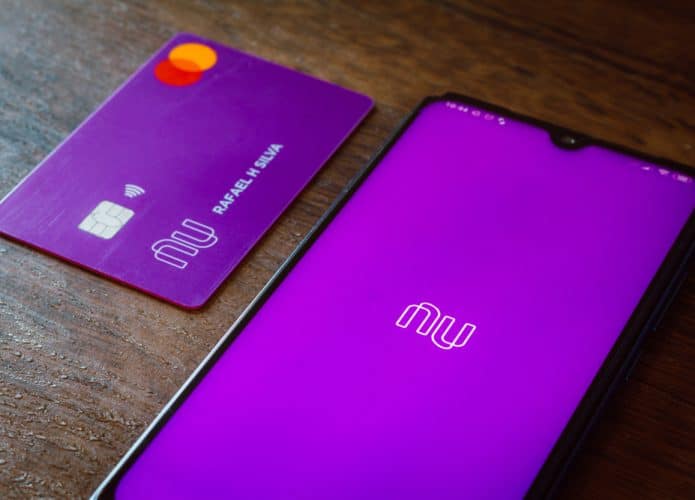 Logotipo do Nubank exibido na tela de um smartphone com um cartão do banco digital ao lado