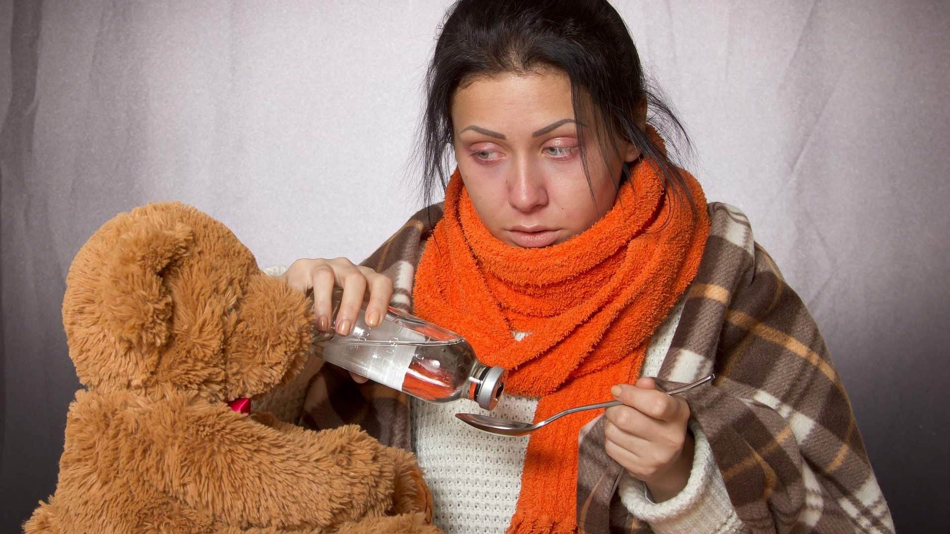pessoa com gripe tomando remédio e com um ursinho de pelúcia ao lado, para ilustarar o ataque do malware FluBot