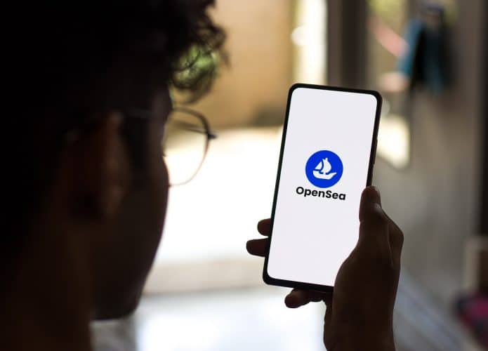 Homem empunhando celular com a marca do OpenSea, maior mercado de NFTs no mundo, no display