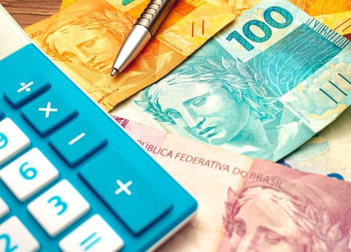 Notas de real brasileiro sobre uma mesa de madeira com calculadora e caneta