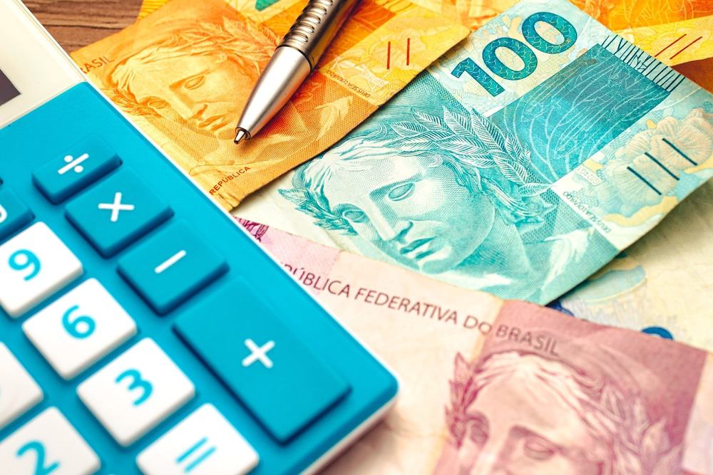 Notas de real brasileiro sobre uma mesa de madeira com calculadora e caneta