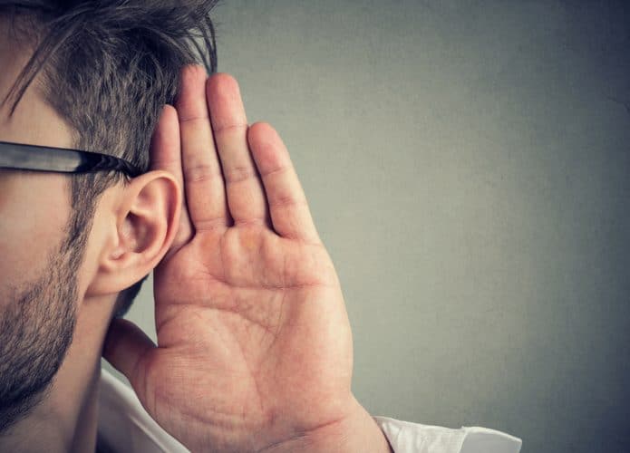 Homem segura a mão perto da orelha e escuta cuidadosamente. Conceito de audiodescrição