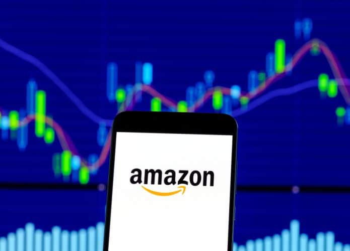Logotipo da Amazon é visto em um smartphone sobre gráficos de ações