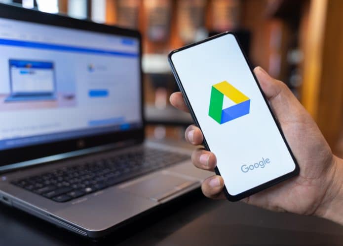 Celular com o logotipo do serviço de armazenamento na nuvem Google Drive com um computador ao fundo
