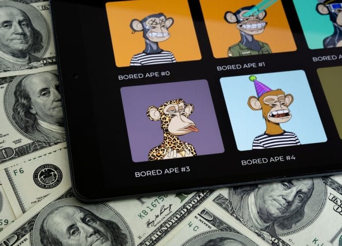 Coleção de NFTs Bored Ape vista na tela de um tablet com notas de 100 dólares ao fundo