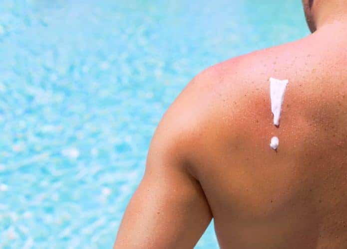 Homem tomando sol com um símbolo de exclamação desenhado com protetor solar nas costas