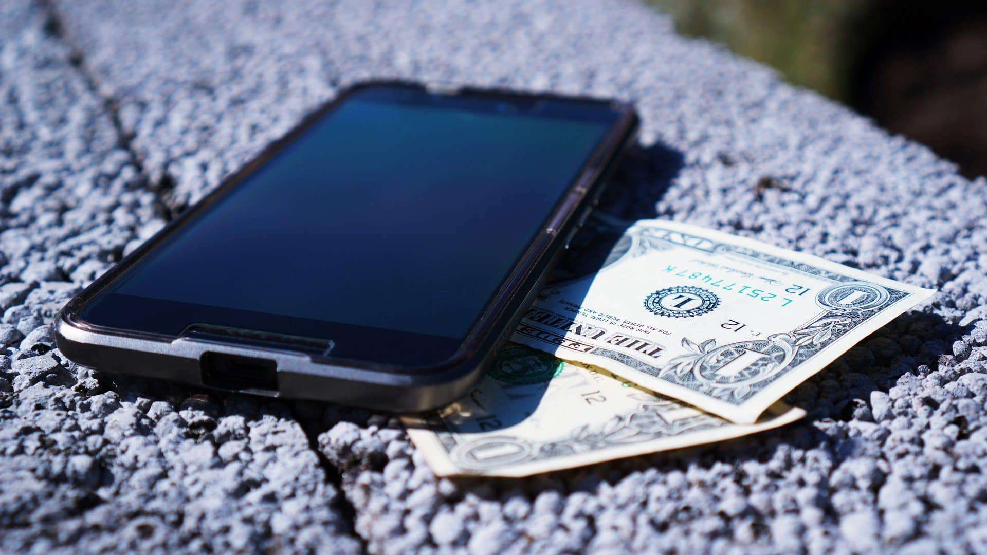 Celular com notas de dólar embaixo para ilustrar que golpes estão usando o serviço Zelle nos Estados Unidos e os bancos não estão ajudando