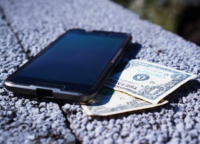 Celular com notas de dólar embaixo para ilustrar que golpes estão usando o serviço Zelle nos Estados Unidos e os bancos não estão ajudando