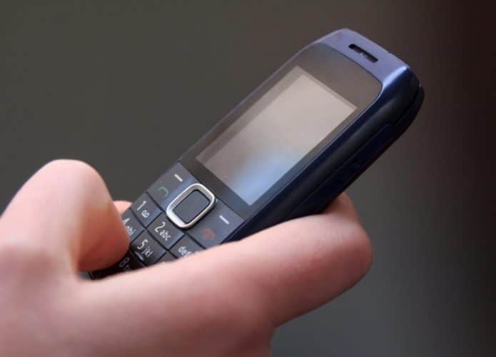 Pessoa enviando mensagens de texto em um celular antigo, teclado T9