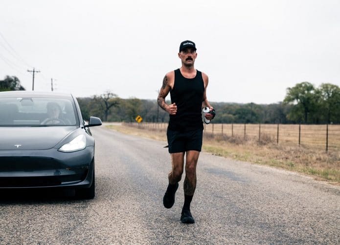 Corredor de ultramaratona enfrentando um Tesla Model 3