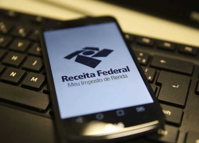 Celular com homepage da Receita Federal aberta em navegador; aparelho está sobre teclado de computador