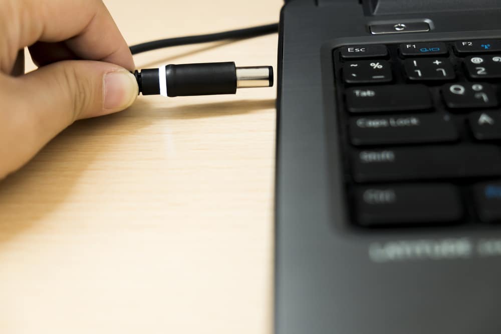 Mão segurando o plugue de alimentação de um notebook.