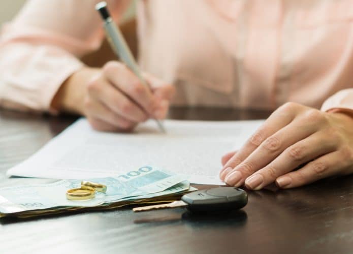 Uma pessoa fazendo cálculos sobre uma mesa com dinheiro e uma chave de veículo para saber o quanto vai gastar com seu carro e tendo em mente a inflação