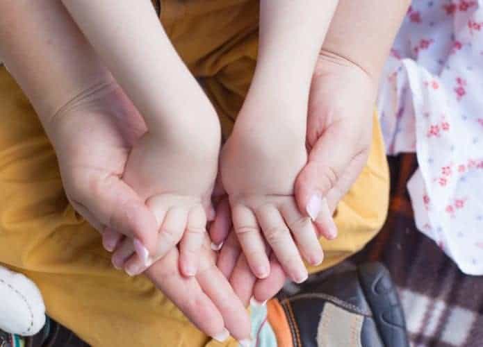 Adulto segurando as mãos de uma criança