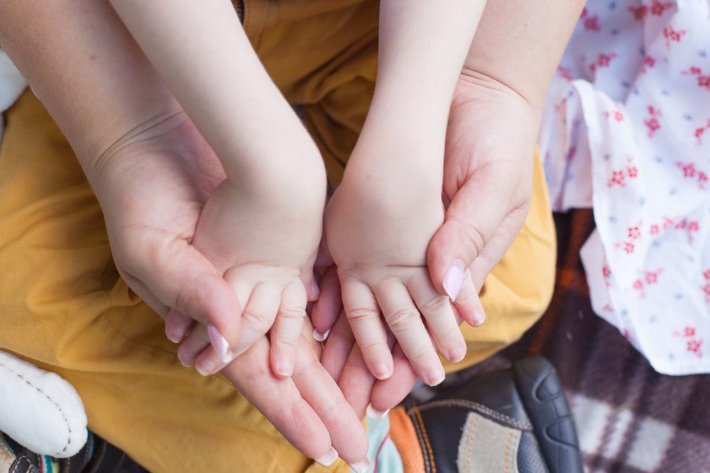 Adulto segurando as mãos de uma criança
