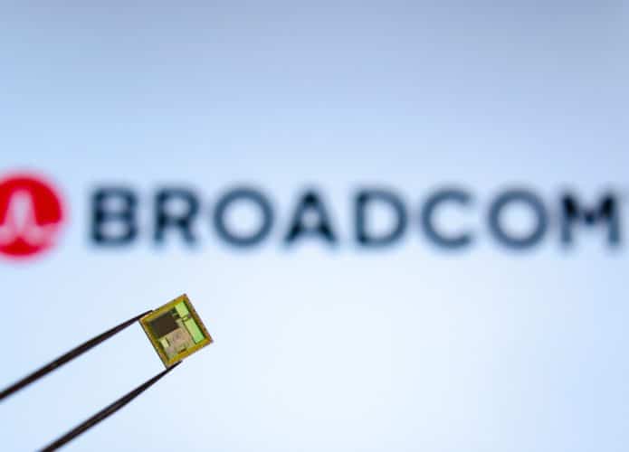 Chip segurado por uma pinça com o logotipo da BROADCOM na tela ao fundo.