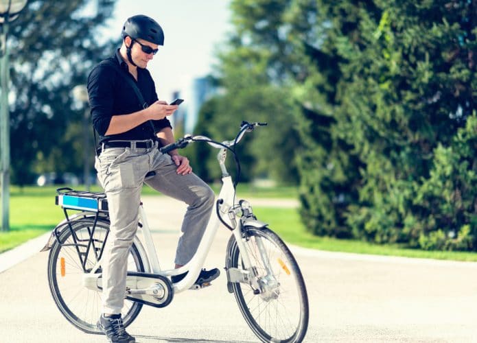Ciclista em uma bicicleta elétrica usando smartphone, para ilustrar uso do aplicativo Apple Maps