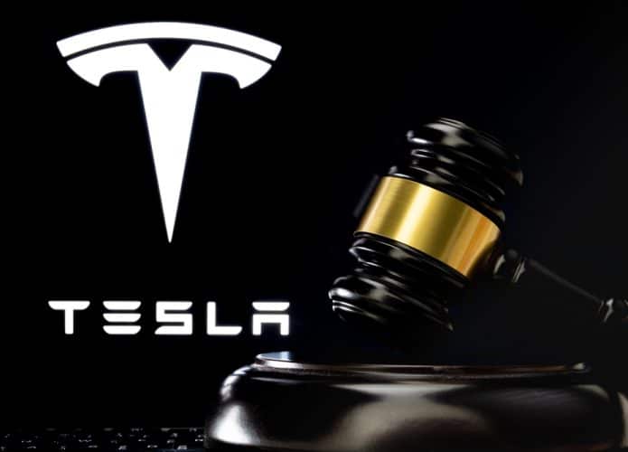 Martelo do juiz na frente e logotipo desfocado da Tesla Company visto na tela atrás.
