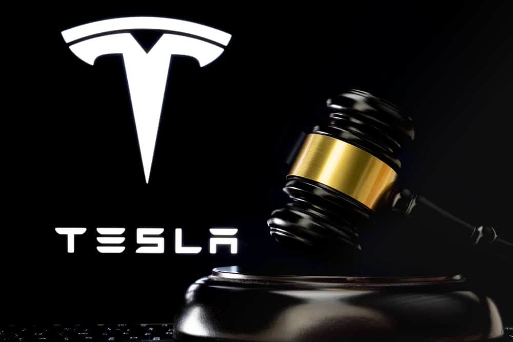 Martelo do juiz na frente e logotipo desfocado da Tesla Company visto na tela atrás.