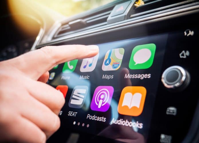 Mulher prestes a pressionar um botão na tela principal do Apple CarPlay no painel de um carro moderno.