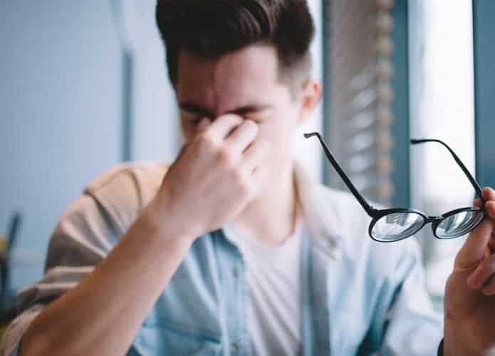 Homem cansado massageando os olhos e segurando seu óculos