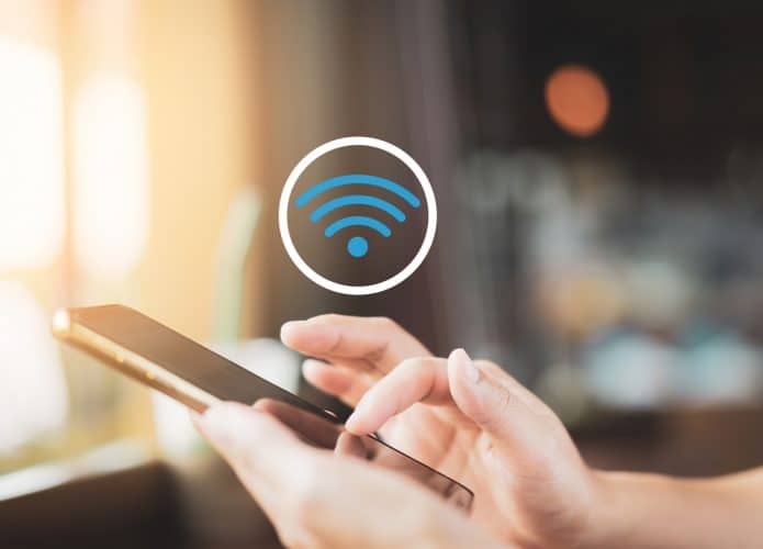Pessoa segurando e usando smartphone abaixo de um logo de Wi-Fi