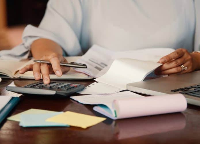 Pessoa fazendo contas usado calculadora e segurando documentos na mesa