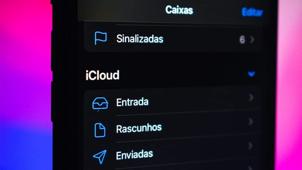 Close num celular com o aplicativo iCloud Mail aberto e um MacBook no fundo
