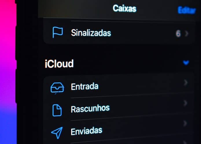 Close num celular com o aplicativo iCloud Mail aberto e um MacBook no fundo