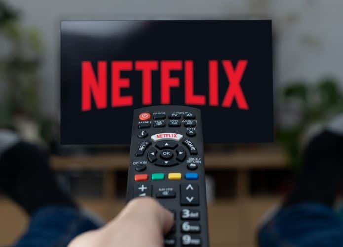 Pessoa apontando controle para TV, que exibe logomarca da Netflix na tela