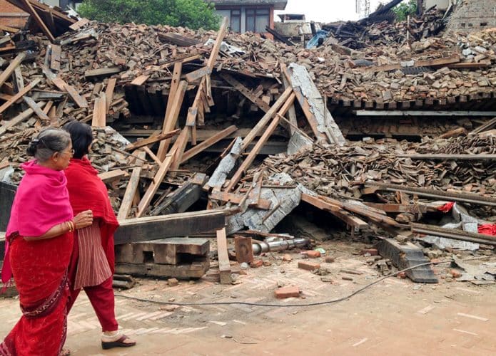 Mulheres caminhando em frente escombros após terremoto no Nepal