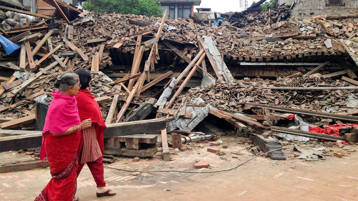 Mulheres caminhando em frente escombros após terremoto no Nepal