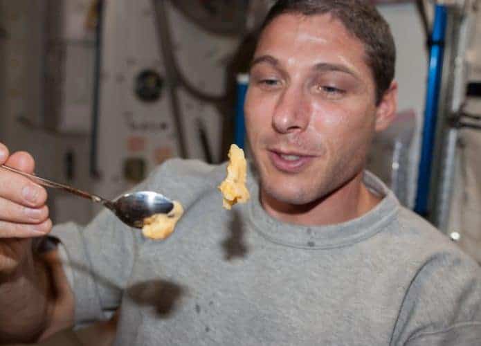 Astronauta segurando colher com comida flutuando na Estação Espacial Internacional