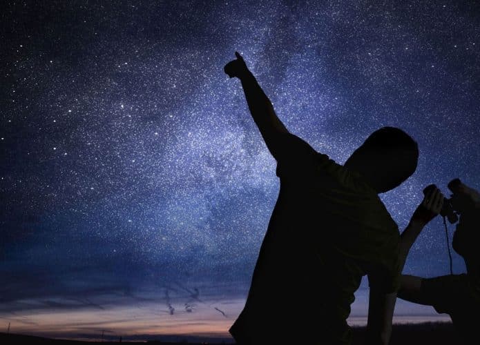 Silhuetas de duas pessoas observando o céu noturno