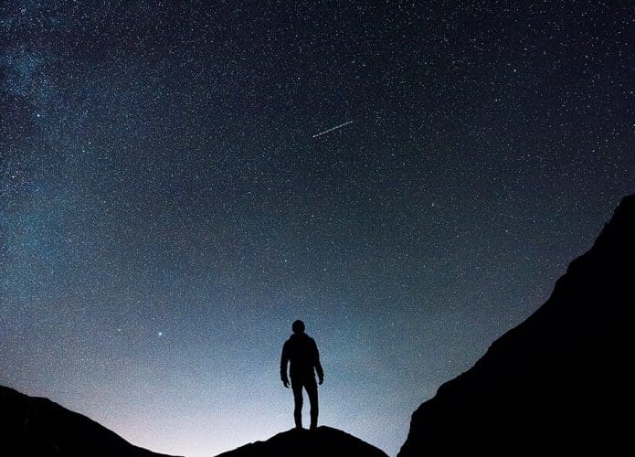 Homem observando estrela cadente em céu estrelado