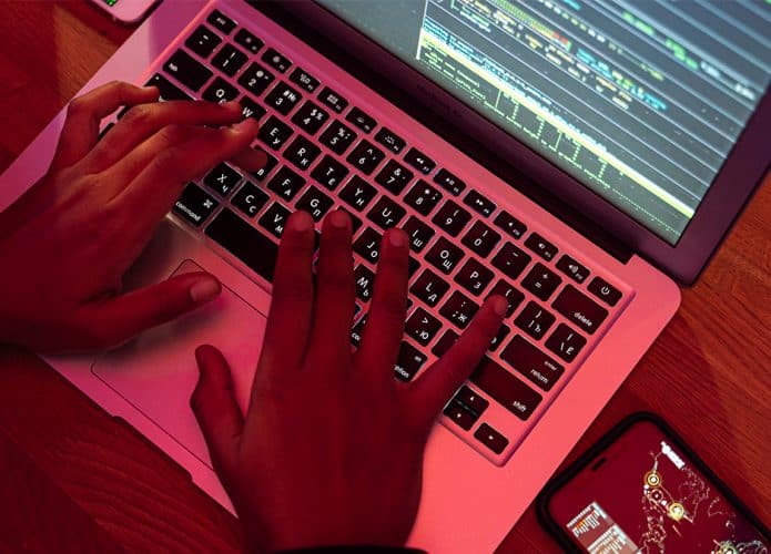 Hacker usando notebook com celular do lado
