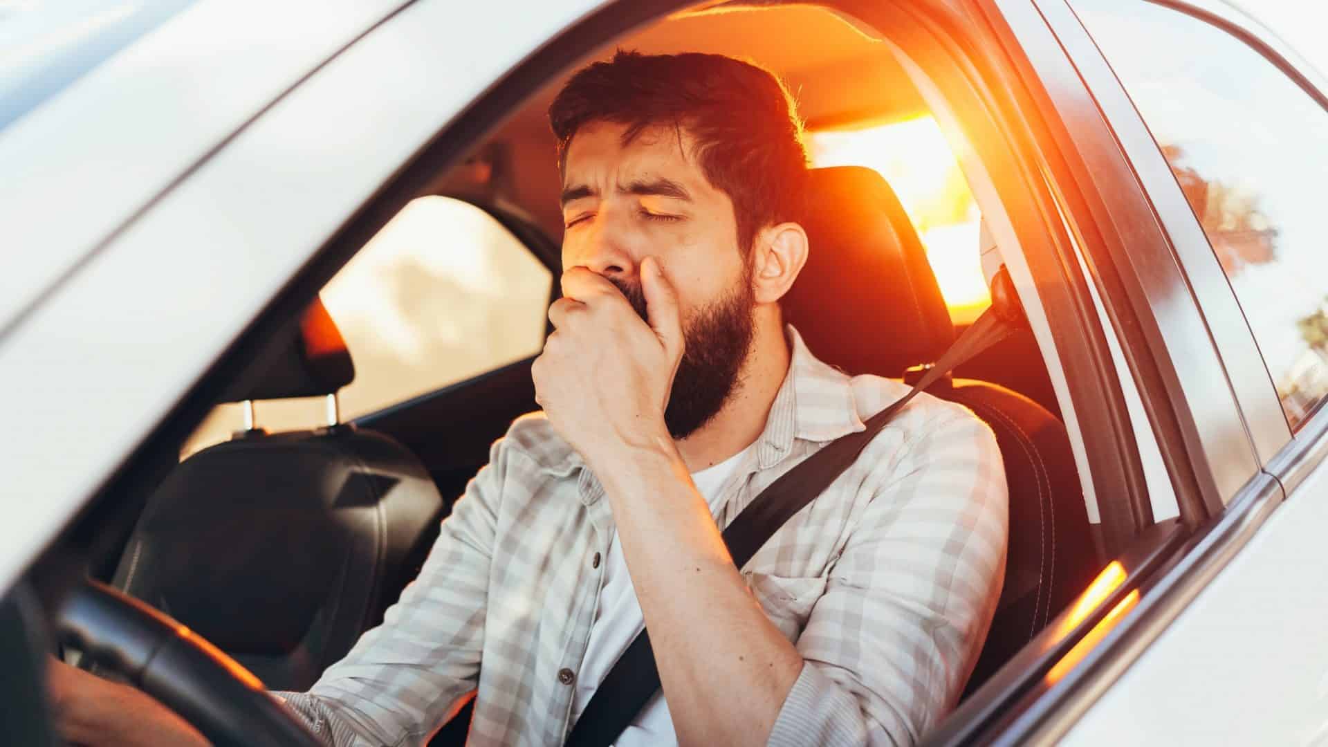 Homem cansado bocejando enquanto dirige seu carro