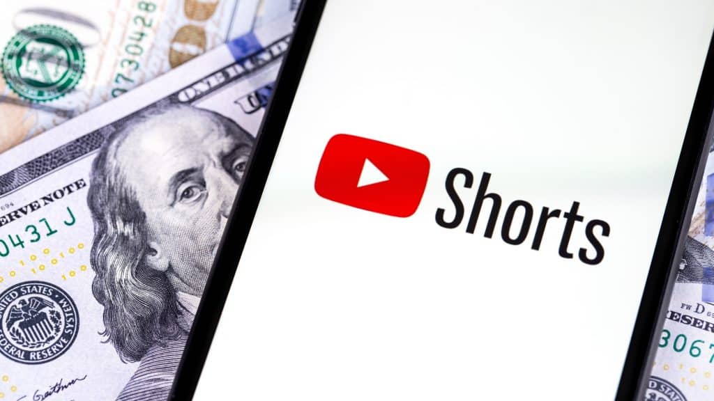 Celular com logomarca do YouTube Shorts na tela em cima de notas de dólar
