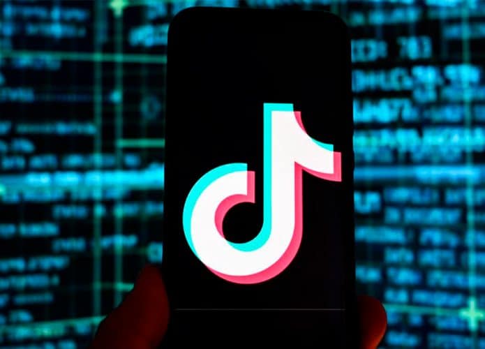 Pessoa segurando celular com logomarca do TikTok em frente tela com linhas de código