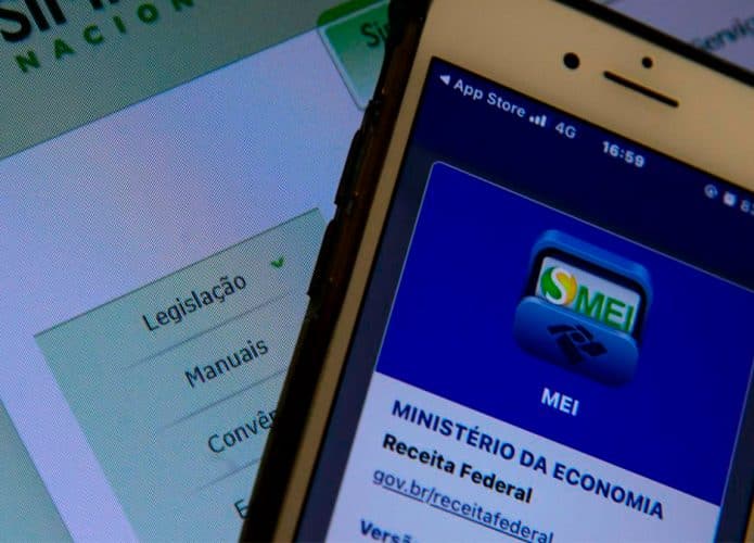 Celular com imagem do MEI em frente a computador com página do Simples Nacional aberta