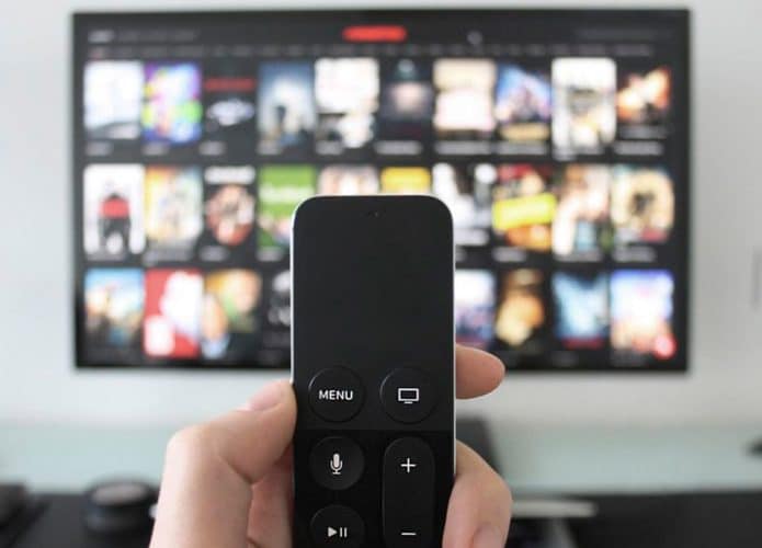 Pessoa segurando controle remoto em frente TV com catálogo de streaming aberto