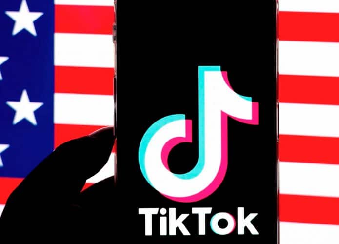 Pessoa segurando celular com logo do TikTok aberto na frente de uma imagem da bandeira dos Estados Unidos